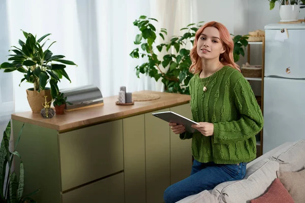 Genç bir kadın yeşilliklerle çevrili güneşli bir yerde tabletle rahatlar..