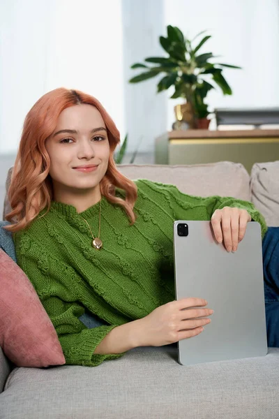 Yeşil kazaklı güzel bir kadın tabletiyle koltukta rahatça oturuyor ve gülümsüyor..