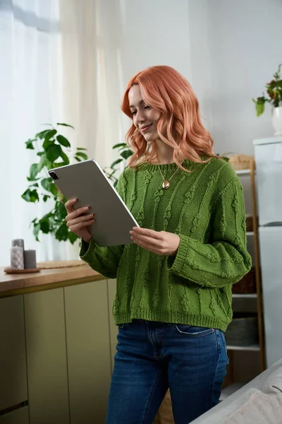 In a peaceful room filled with plants, a cheerful young woman engages with her tablet, smiling.