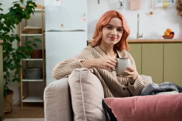 Gül gibi saçları olan genç bir kadın kanepede rahatlıyor, içkisiyle nazik bir anın tadını çıkarıyor..