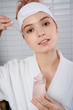 Huzurlu bir ortamda, genç bir kadın su serumunu damlatan, ışıldayan bir güzellikle uygular..