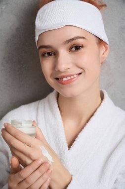 Genç bir kadın, sakin bir spa atmosferine cilt kremi sürerken nazikçe gülümser..