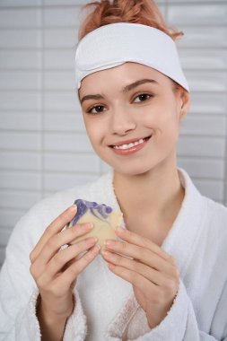 Genç bir kadın, huzurlu bir banyoda renkli bir el yapımı sabun tutuyor..