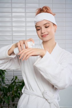 Yumuşak bornozlu genç bir kadın, sakin bir kaplıca ortamında ellerine losyon sürüyor..