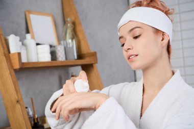 Sakin bir banyoda, genç bir kadın nemlendirici sürüyor, huzur saçıyor..