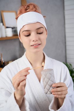 Huzurlu bir odada, güzel genç bir kadın nazikçe gülümserken dikkatlice bir mum yakar..