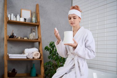 Genç bir kadın rahatlatıcı bir kaplıcada, rahat bir bornozla otururken cilt bakımı yapıyor..