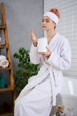 Güzel, genç bir kadın sıcak bir banyoda huzur içinde oturur ve kendine bakmanın tadını çıkarır..