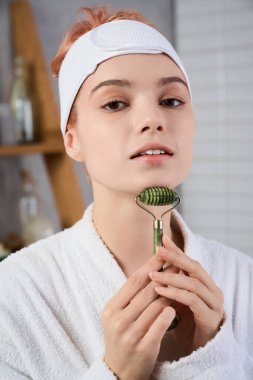 Genç bir kadın parlayan cildinde yeşim bir silindir kullanıyor, sakin bir yerde kendine dikkat ediyor..