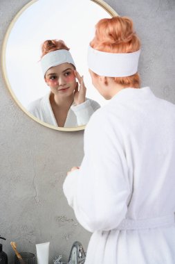 Sakin bir banyoda, genç bir kadın yuvarlak bir aynada tenini güçlendirir..