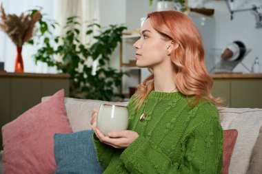 Büyüleyici saçları olan genç bir kadın sıcak içkisinin tadını çıkarıyor, büyüleyici bir ev atmosferiyle çevrili..