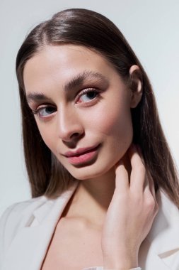 Uzun saçlı zarif bir genç kadın nazikçe boynuna dokunuyor, kendine güveni ve cazibesi tam..