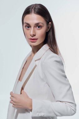 Işıl ışıl cildi olan genç bir kadın ceketini zarif bir şekilde ayarlıyor..