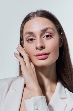 Genç bir kadın yüzüne dokunur, kendine güveni ve zarafetiyle şık bir elbise giyer..