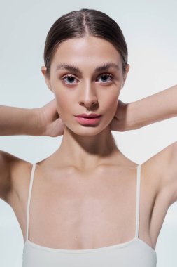 Genç bir kadın zarafet ve duruş sergiliyor, hafifçe saçlarını geriye doğru tutarak doğrudan ileriye bakıyor..