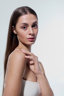 Uzun saçlı genç kadın nazikçe omzuna dokunuyor. Yumuşak ışıkta zarafet ve cazibe saçıyor..