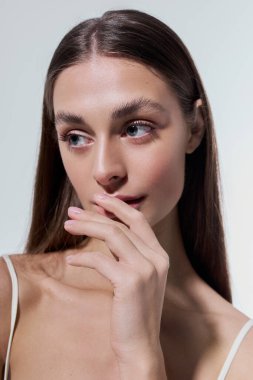 Genç, güzel bir kadın nazikçe dudaklarına dokunuyor, narin ışık altında sakinlik ve zarafet yayıyor..