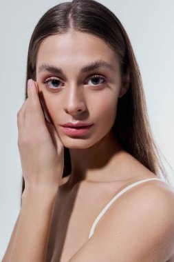 Genç bir kadın yanağına hafifçe dokunuyor, doğal güzelliğini ve zarafetini sergiliyor..