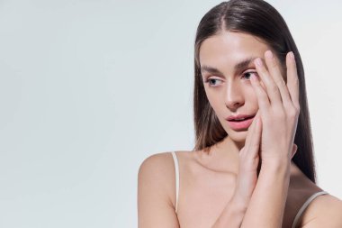 Güzel, genç bir kadın usulca poz verir, büyüleyici ifadesi ve büyüleyici elleri vardır..