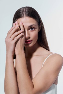 Genç bir kadın, bir eli yüzünün yanında yumuşak bir tonda tutarak çarpıcı güzelliğini açığa vurur..