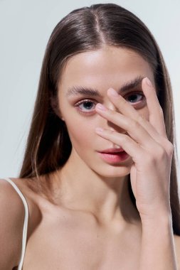 Sevimli genç bir kadın elleriyle yüzünü gizliyor. Yumuşak ışıkta ışıldıyor..