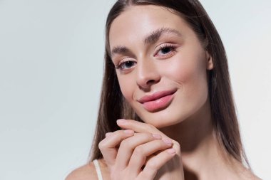 Güzel genç bir kadın nazikçe poz verir, zarafeti somutlaştırır ve yumuşak ışıkta durur..