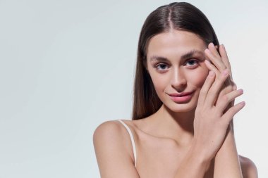 Sevimli genç bir kadın yüzüne hafifçe dokunurken sıcacık gülümser. Güzellik ve kendine güven saçar..