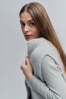 Güzel genç bir kadın zarif bir şekilde duruyor, süveterini minimalist bir şekilde tutuyor..