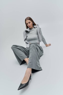 Gri elbiseli, kendine güveni ve cazibesi olan güzel bir genç kadın zarif bir şekilde poz verir..