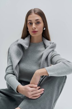 Sade gri elbiseli genç bir kadın zarif bir ifade sergiliyor..