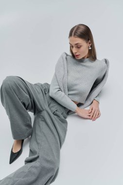 Göz kamaştırıcı genç bir kadın otururken şık gri bir elbiseyle moda anlayışını sergiliyor..