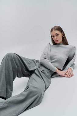 Genç bir kadın kendine güven ve zarafet saçar, zarif bir şekilde poz verirken şık gri elbiseler giyer..