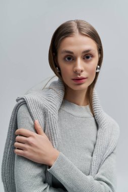 Gri kazaklı ve küpeli kendine güvenen genç bir kadın zarafet saçar..