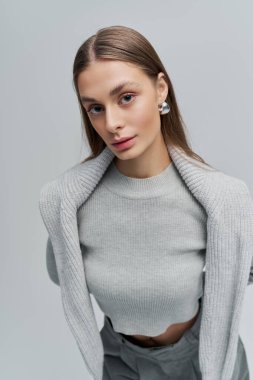 Bu genç kadın tarzını gri bir kazak ve şık küpelerle gösteriyor..