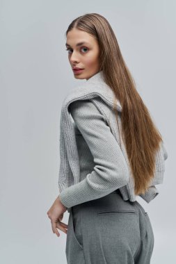 Şık bir genç kadın zarif bir şekilde ayakta duruyor, uzun saçlarıyla ve şık elbisesiyle hava atıyor..