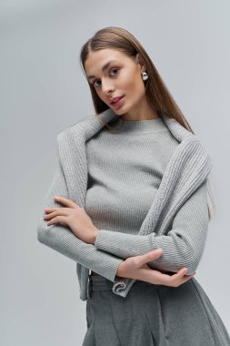 Uzun saçlı genç bir kadın zarif gri bir elbise içinde kendine güvenini yayıyor..