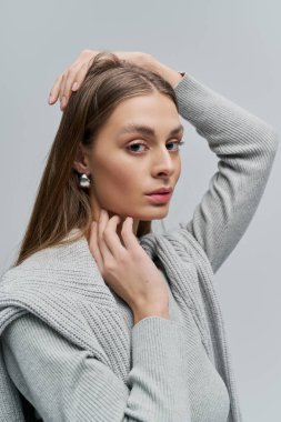 Uzun saçlı genç bir kadın şık gri elbiseler ve zarif bir duruş sergiliyor..