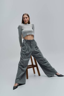 Güzel, genç bir kadın, ahşap bir taburede dimdik dururken modern moda sergiliyor..