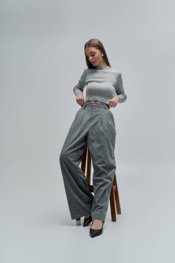 Güzel genç bir kadın, ahşap bir tabureye oturmuş modern modaya özgüvenini sergiliyor..