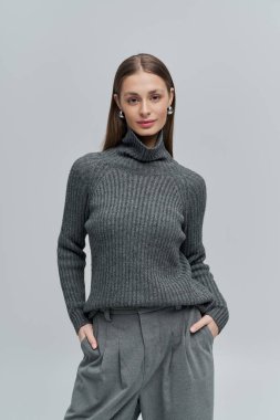 Şık gri kazaklı ve özel dikim pantolonlu şık bir genç kadın zarif bir şekilde duruyor..