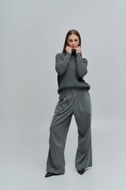 Göz kamaştırıcı genç bir kadın basit bir arkaplana karşı şık bir elbiseyle rahatça poz verir..