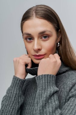 Gri kazaklı hoş genç bir kadın nazikçe yakasına asılıyor.