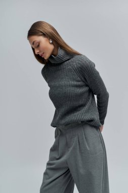 Güzel, genç bir kadın zarif, gri bir elbise içinde, kendine güvenen bir şekilde poz verir..