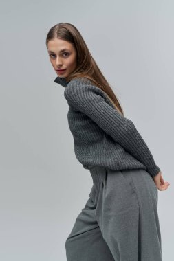 Şık, genç bir kadın şık, gri bir elbiseyle özgüven yayar. Zarif bir poz verir..