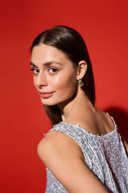 Güzel genç bir kadın, zarafetle omzunun üzerinden bakıyor, koyu kırmızı renklerle çevrili..