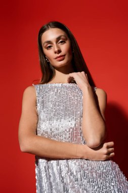 Göz kamaştırıcı genç bir kadın zarif bir yüz ifadesiyle, parıldayan bir elbise giyerek ayakta duruyor..