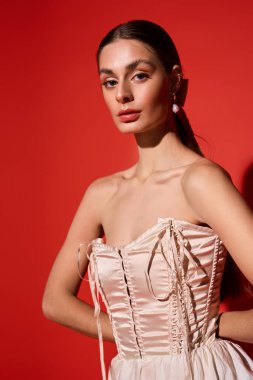 Genç bir kadın canlı kırmızı bir arka planda çarpıcı bir elbiseyle rahatça poz veriyor..