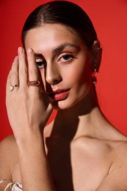 A striking young woman showcases fine jewelry against a bold red backdrop.