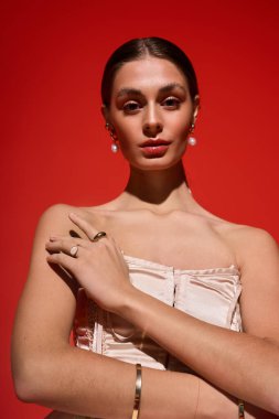 Kendine güvenen genç bir kadın kırmızı bir arka plana karşı kollarını kavuşturmuş duruyor..