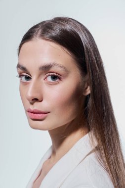 Uzun saçlı genç bir kadın özenle bakıyor, kusursuz cildini ve zarafetini sergiliyor..